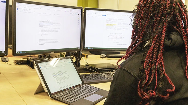 A black student with red braids is looking at her laptop and computer during class EGR 102