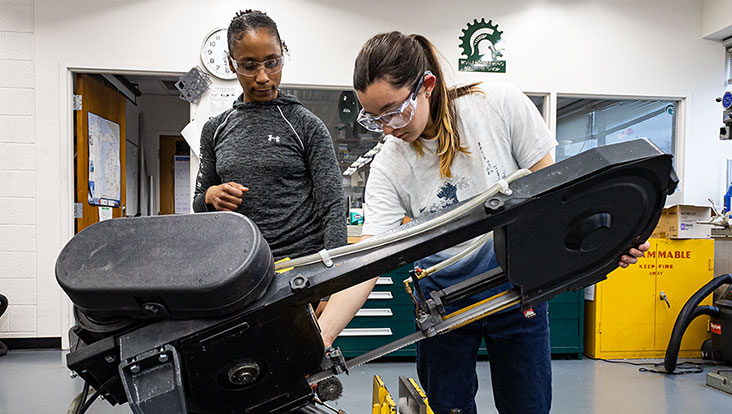 Students working on a heavy cutting machine in a women’s workshop.