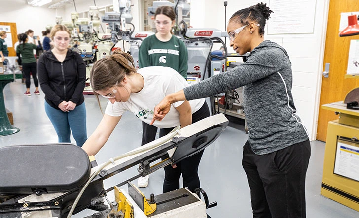 Black and white female undergraduate students working on a mechanical machine during a workshop