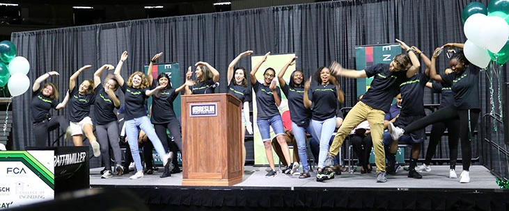Diverse undergraduate student CoRe Ambassadors dancing on stage during Colloqium