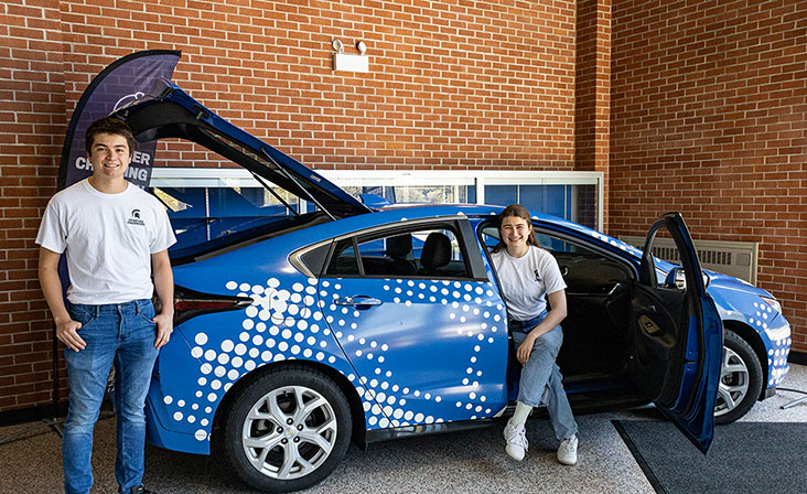 Students in the EV Scholar car, one standing and one sitting.