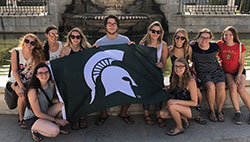 MSU student group holding a flag with the spartan helmet in front of a building in Madrid spain