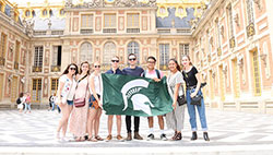 MSU Engineering student group holding a flag with the spartan helmet on it, standing in front of a building at CEA Paris Center
