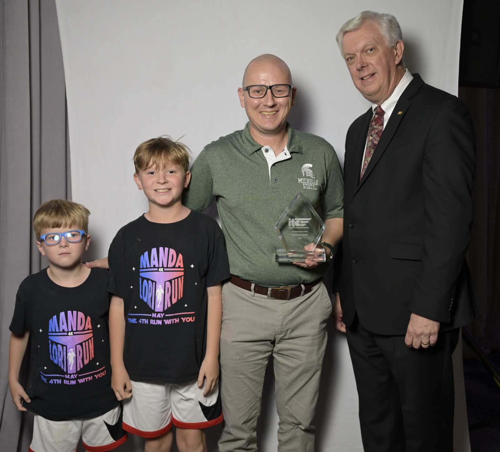Sami and Olin stand with their dad, Peter Savolainen, after he received the 2024 ITE Council Impact Award from ITE President John Davis.