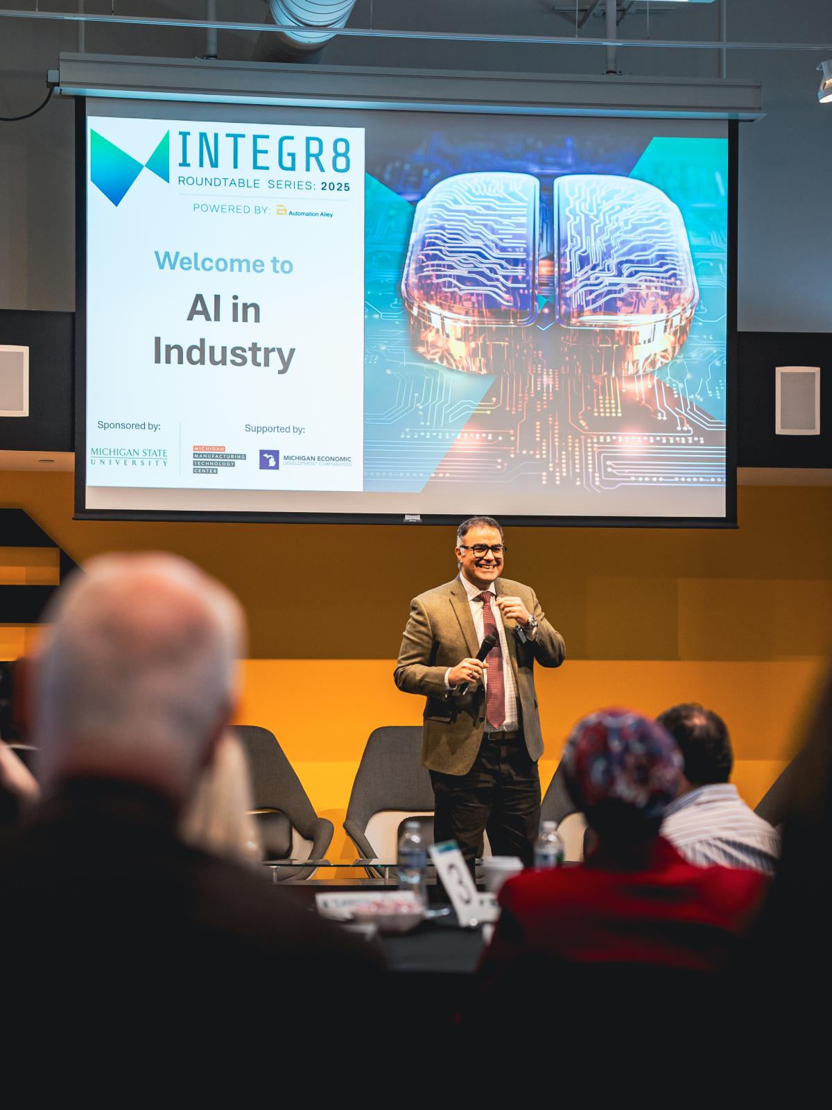 Man in a suit presenting on a stage with graphic reading