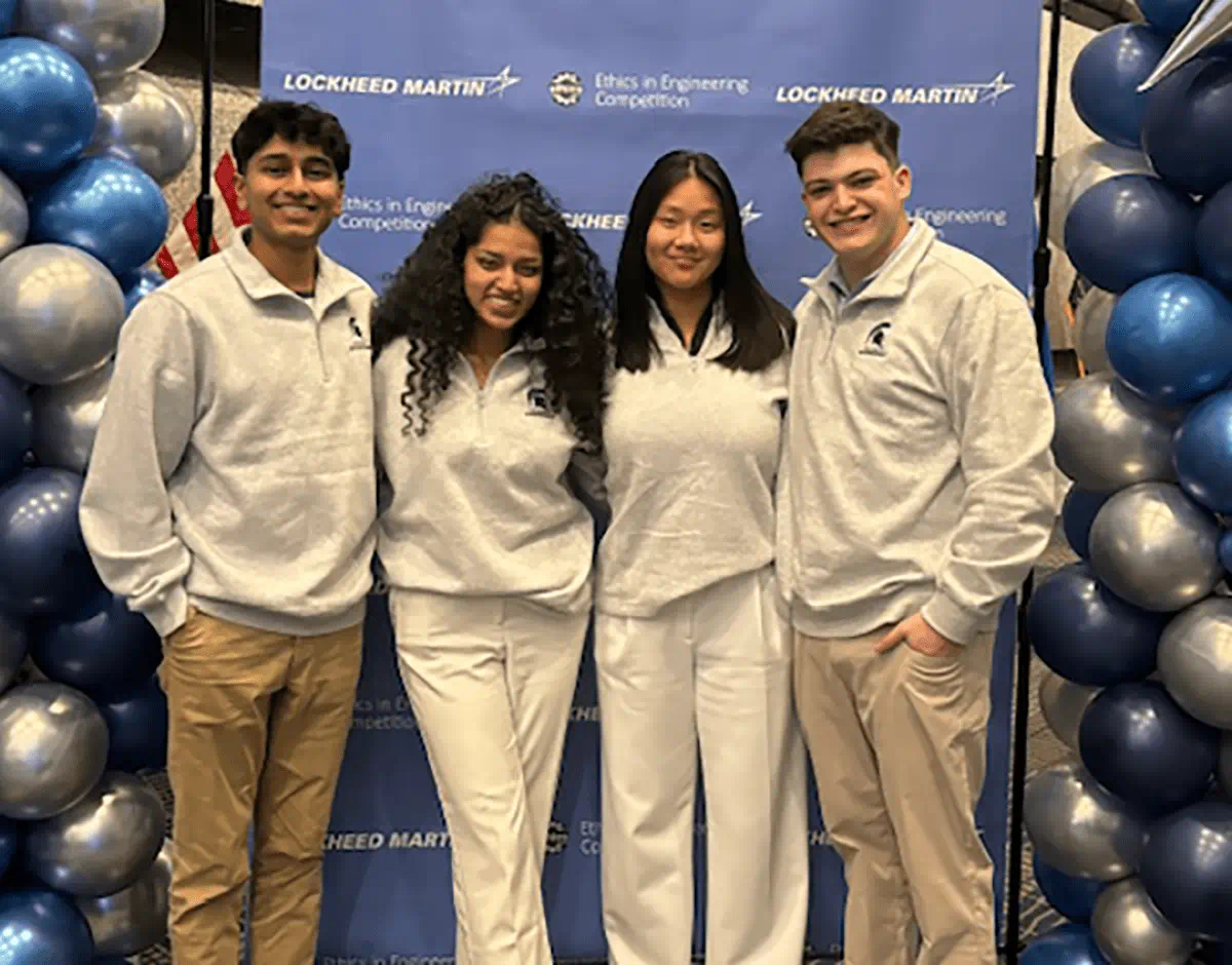 Four people posing in front of a backdrop, flanked by blue and silver balloons.