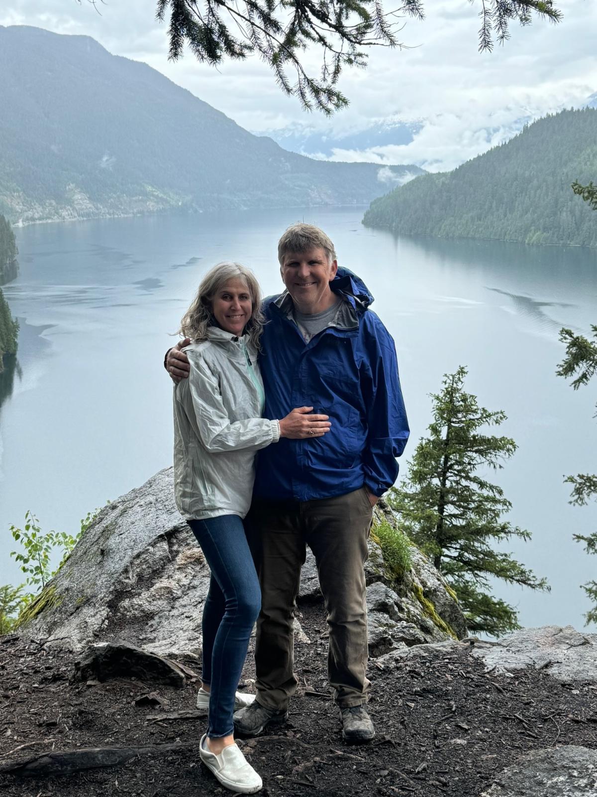 Meryl Katz and Jack Peurach smiling at the camera with a beautiful lake and mountains in the background.