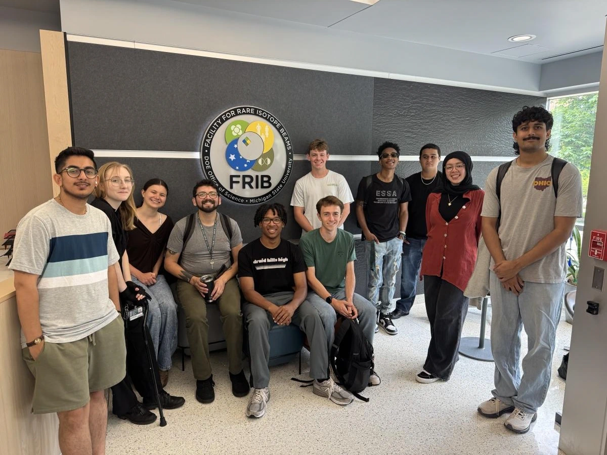 REU cohort smiling and posing in front of the FRIB sign.