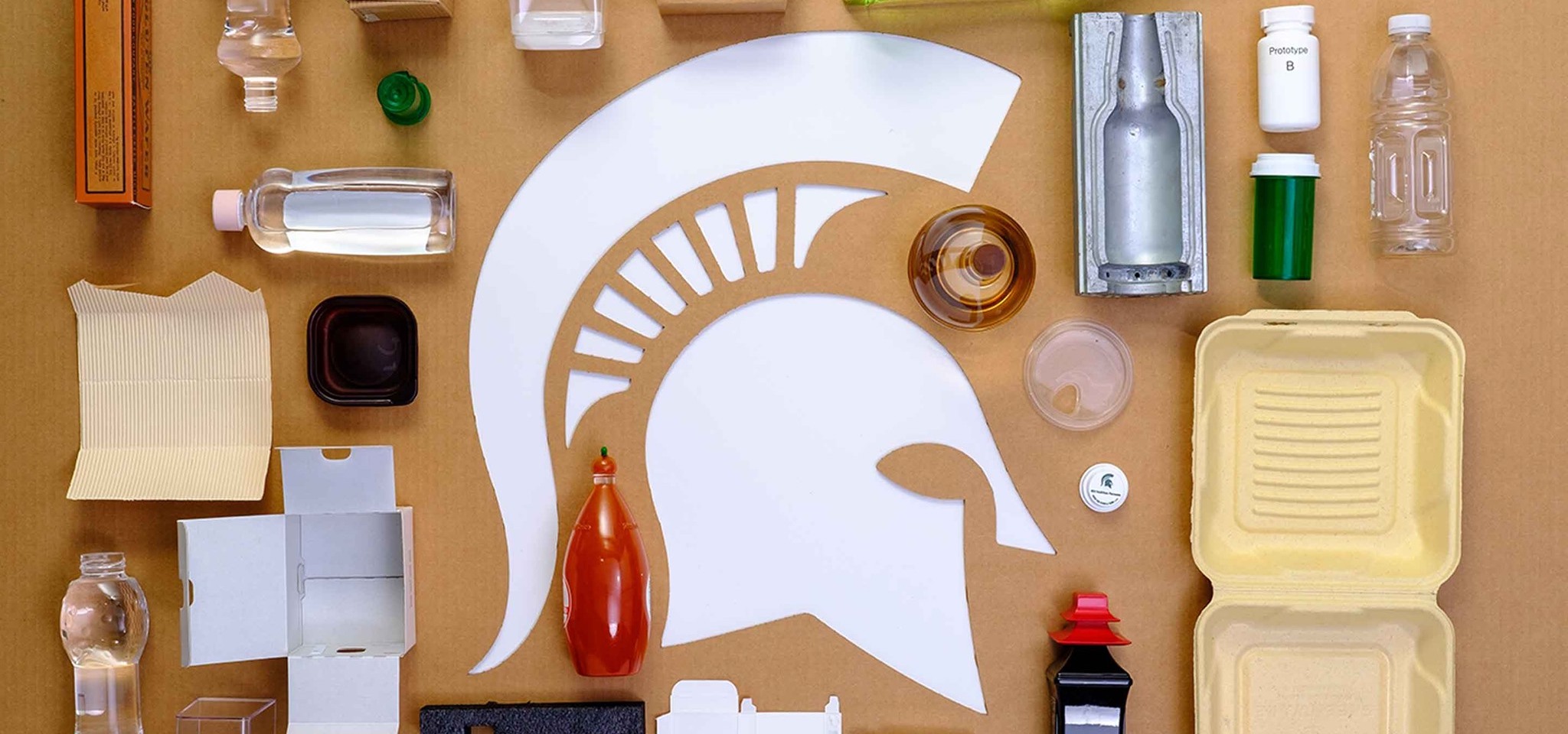 A spartan helment cutout in cardboard, and on top of the cardboard surrounding the cutout are multiple packaging materials in forms of bottles, casts, boxes