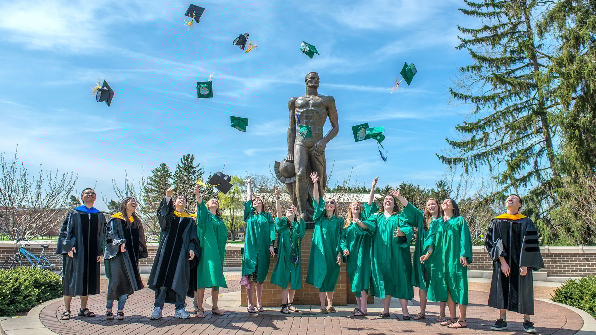 Graduates throwing caps in air in front of the Spartan Statue