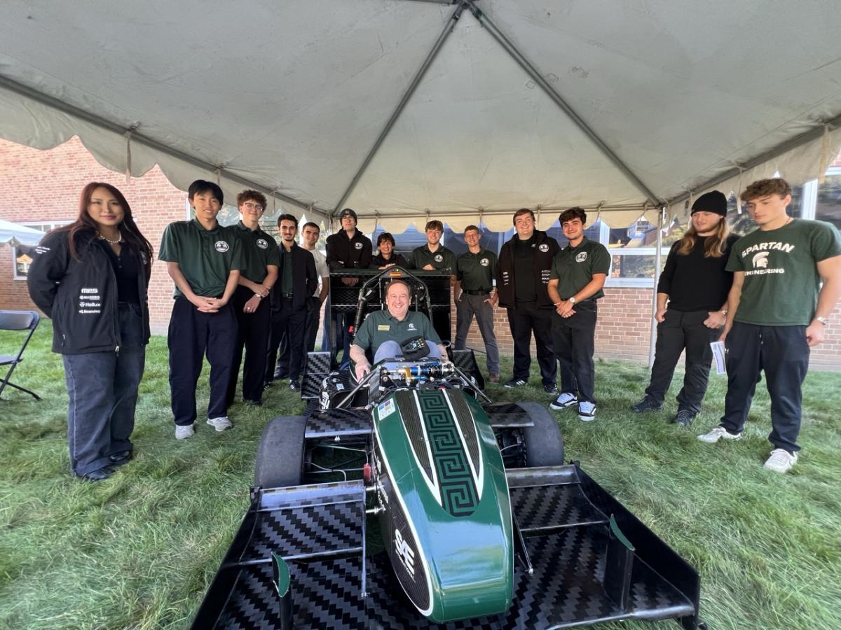 Dean John Papapolymerou sits in a Michigan State Formula Racing car surrounded by student team members during the 2026 Engineering Colloquium.