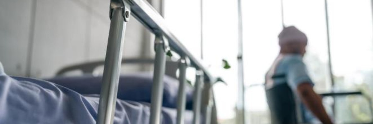 A person seated in a wheelchair rests beside a hospital bed in a bright clinical room