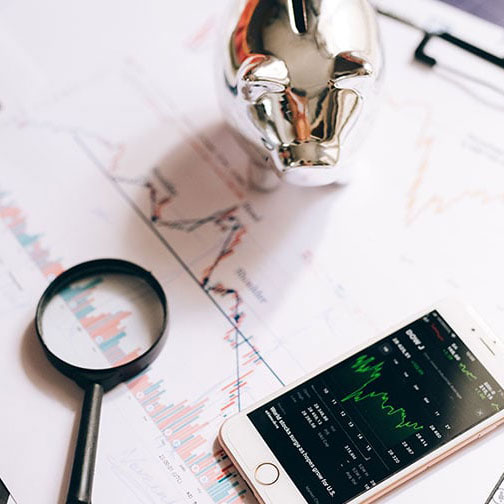 Stock market app on a phone next to a piggy bank and a microscope over a sheet with a graph