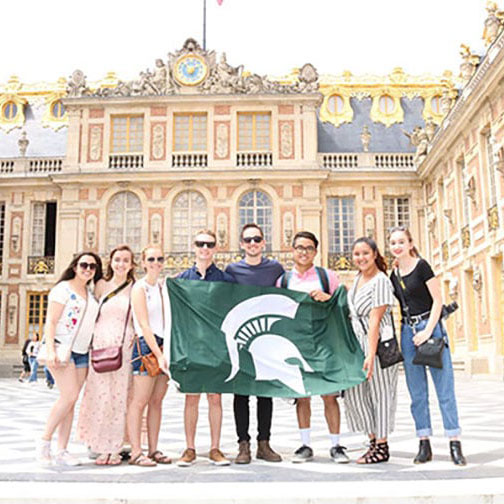 Student group holding a Spartan flag in front of the CEA Paris Center building