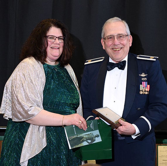 Geoff Gavrila in a veteran?s uniform holding an award next to Laura Genik