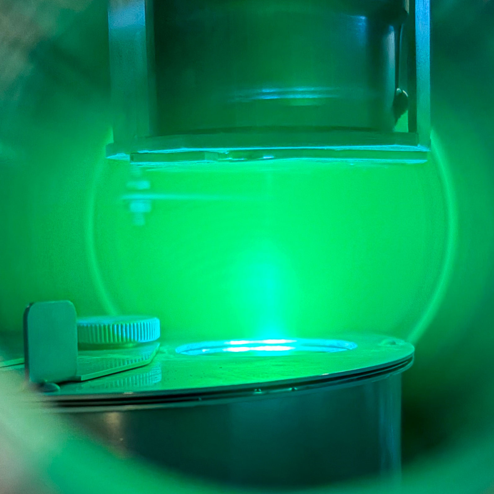 In this picture, the Mg2SiO4 target in the sample carousel at the bottom of the picture is  being hit by a rastering 248 nm KrF excimer pulsed laser deposition (PLD) laser beam, the substrate upon which the Mg2SiO4 film is being grown (which you can't see) is attached to the underside of the rotating heater assembly at the top of the picture, and the plasma is in between (Nicolas)​