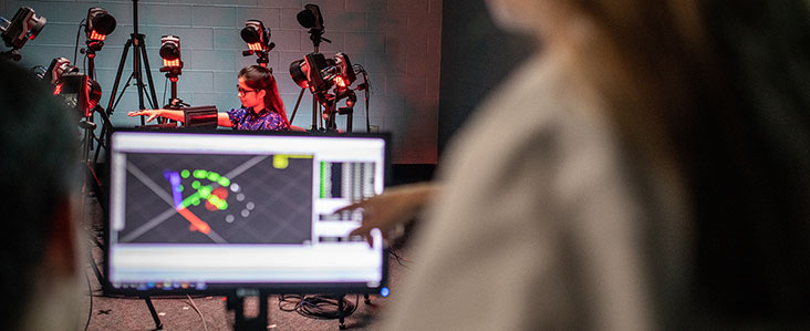 Mechanical engineering students looking at a computer screen with a student wear some mechanical sensors that are displayed on the computer