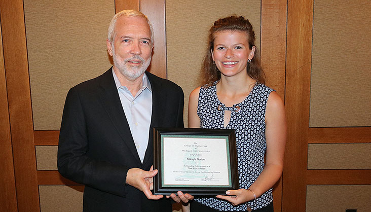 Student stands with Von Ehr while holding a scholarship certificate