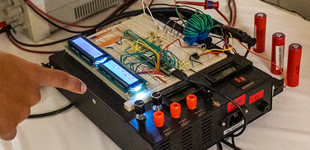 Student pointing at their capstone project, the project is a machine with batteries