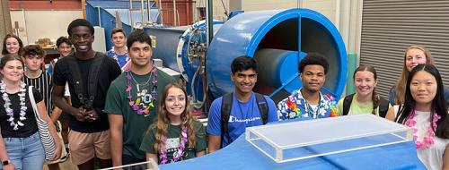 a wide range of multi-cultural students standing in a lab in front and behind two blue machines during a ESSA event